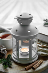 Lantern with burning candle and winter decor on wooden tray