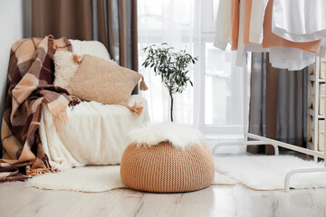 Interior of cozy living room with pouf, chair and clothes