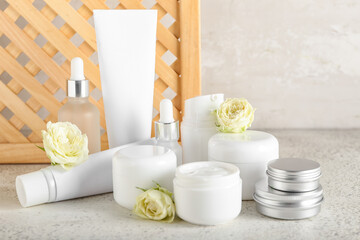 Different cosmetic products and flowers on light background