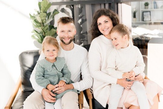 Portrait of beautiful stylish family with little children looking at the camera and smiling. Happy parents sitting at chairs with lovely small daughter and joyful son, enjoying moments together