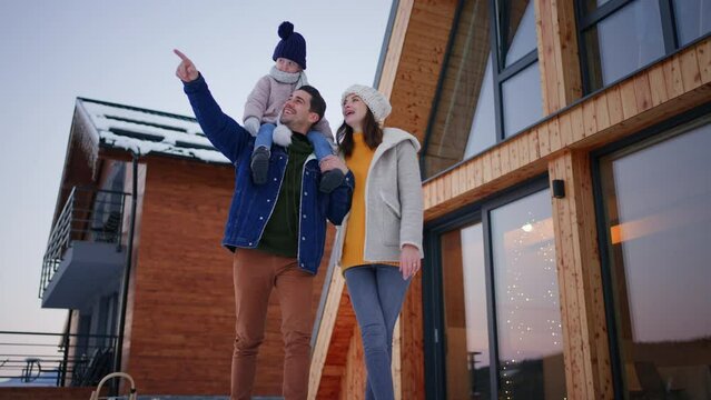 Low angle view of happy young family on holiday with small child standing in front of cabin in winter.