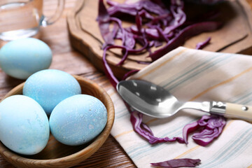Bowl with natural dyed Easter eggs and purple cabbage on wooden table, closeup