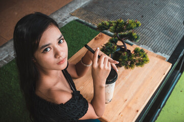 A pretty Filipino girl in an off shoulder black top with a cup of milk tea at a small al fresco cafe.