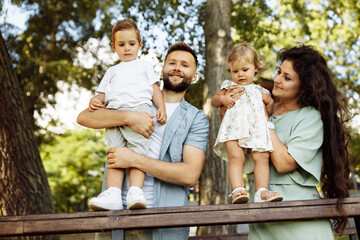 Happy family with small kids spending weekends together at the park, smiling. Caring mother and father cuddling with little daughter and son, enjoying joyful moments, parenthood concept
