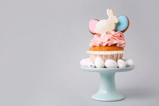 Stand with tasty Easter cupcake and eggs on grey background