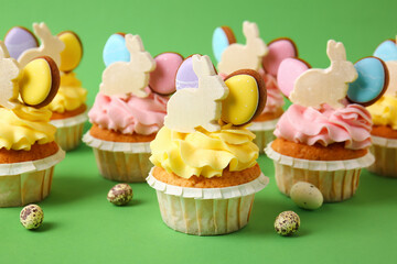 Tasty Easter cupcakes and eggs on green background, closeup