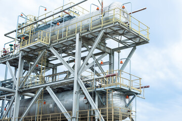 Two metal containers stand against the background of a gas processing plant.