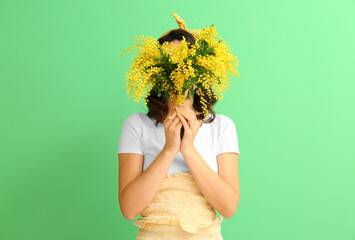 Beautiful young woman with bouquet of mimosa flowers on green background - obrazy, fototapety, plakaty