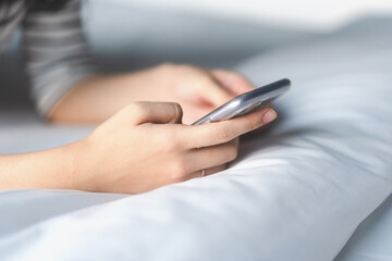 Woman hand using mobile phone on bed.