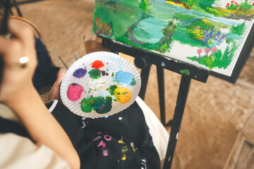 Woman painting brush on canvas at workshop art lesson class focus on palette.