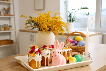 Tray with Easter cakes, eggs and burning candle on kitchen counter