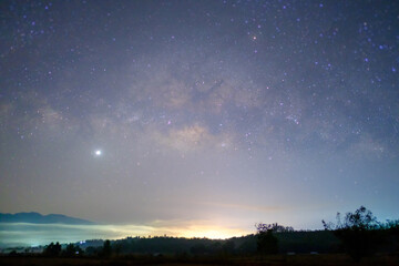 Long exposure shot of the Milky way in the sky over the hillside city light at Northern Thailand.