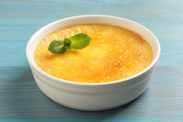 Delicious creme brulee with mint on light blue wooden table, closeup view