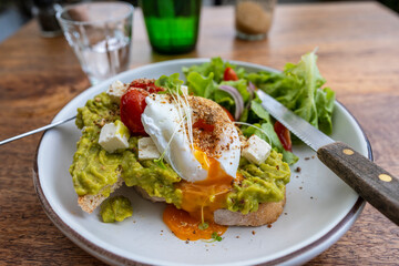 Sourdough toast, poached eggs, avocado pulp and fresh vegetables on plate in cafe, close up