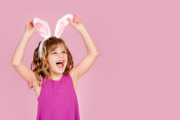 Easter concept - happy little caucasian girl raise head up touching bunny ears headband over pink background and looking away, copy space 