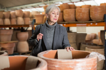 Gray haired woman selecting decorative earthenware pot in home goods store.