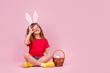 Little beautiful smiling girl in Easter bunny ears headband holds in hand a basket with Easter...