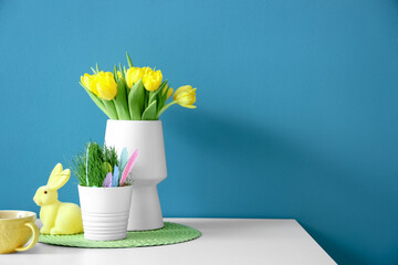 Vase with tulips, Easter decor and cup on table near color wall