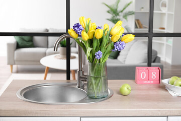 Kitchen counter with flowers, cube calendar, modern sink and fresh apple. International Women's Day celebration