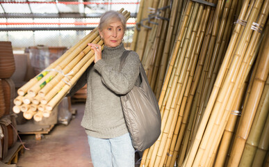 Senior woman carrying bunch of bamboo poles while shopping in home goods store.