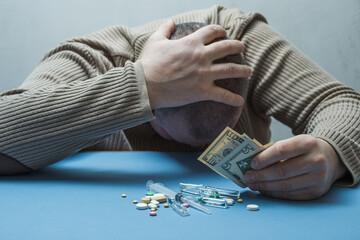 The man hides his face with one hand, holds money in the other, and medical preparations are in...
