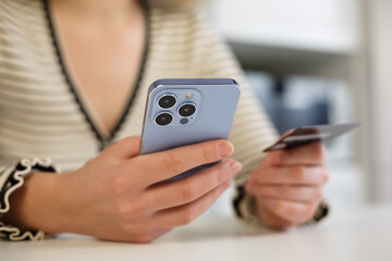 Young woman buying online with credit card and mobile phone app. Female making money transfer with bank card and modern smartphone device with triple camera. Customer making purchase in internet store