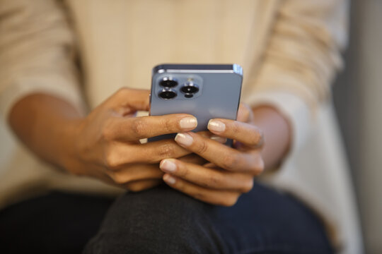 Young black woman texting in messenger app on smartphone. African female using modern blue mobile phone for communication online. Person holding new cellphone with triple camera - Powered by Adobe