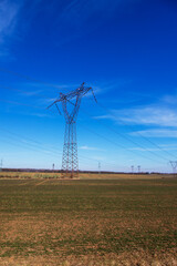 High voltage poles for electricity distribution in the countryside. In the background is a blue sky with dramatic clouds.