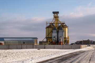 agro silos granary elevator in winter day in snowy field. Silos on agro-processing manufacturing plant for processing drying cleaning and storage of agricultural products, flour, cereals and grain.