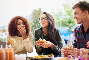 Good food and laughter go hand-in-hand. Cropped shot of three friends eating burgers outdoors. - obrazy, fototapety, plakaty