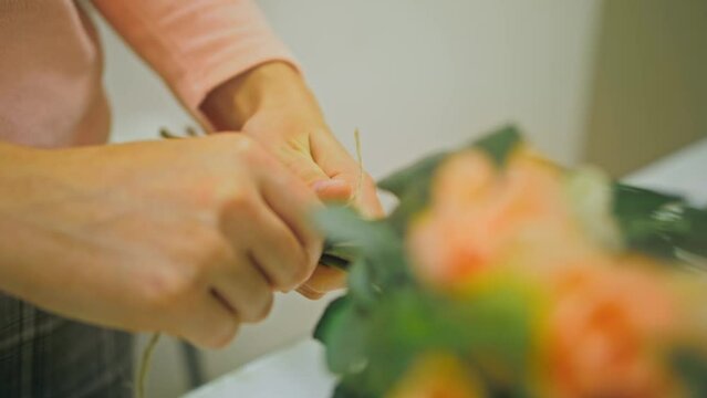 Female florist makes flower bunch, she cuts off wrapping paper working in flower shop. Cute young caucasian professional makes bouquet for sale in floral store. Floristry handmade small business