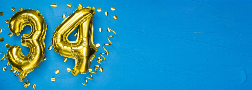 golden foil balloon number thirty four. Birthday or anniversary card with the inscription 34. blue concrete background. Anniversary celebration. Banner.