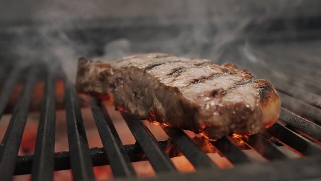 Roasting juicy meat steak with spices and herbs in burning charcoals fire on bbq grid, flames and smoke. Barbecue grill