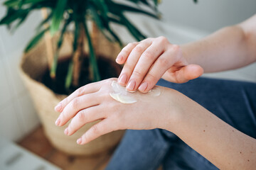 Woman smears a moisturizing hand cream on hand's skin. home body care and healthy lifestyle.