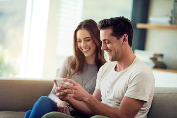 Sharing is caring. Shot of a happy young couple using a phone together on the sofa at home.