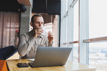 A young smart man is sitting in the office with a cup of coffee and is working on a project related to public cyber technology. Businessmen with laptop trying to meet deadlines in external marketing.