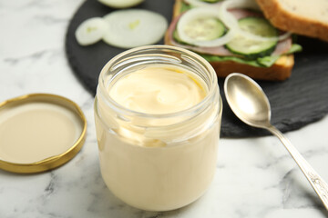Obraz na płótnie Canvas Jar of delicious mayonnaise near fresh sandwich on white marble table