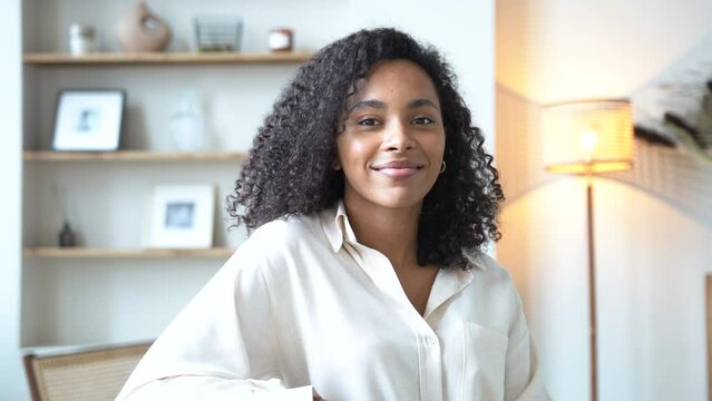 Cheerful ethnic woman relaxing on sofa at home. Successful young african woman with toothy smile sitting on couch and looking at camera. Portrait of confident black woman laughing.