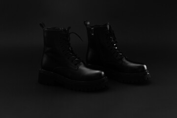 Pair of isolated leather unisex winter autumn boots of black color on black background. Boots with...