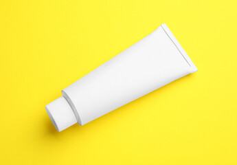 Blank white tube of ointment on yellow background, top view. Space for text
