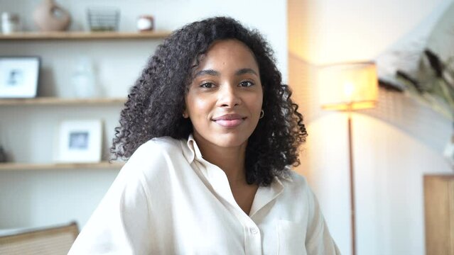 Cheerful ethnic woman relaxing on sofa at home. Successful young african woman with toothy smile sitting on couch and looking at camera. Portrait of confident black woman laughing.