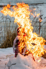burning Maslenitsa doll on snow in the dried grass