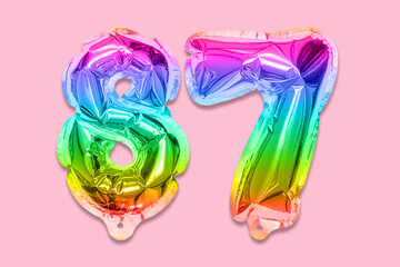 Rainbow foil balloon number, digit eighty seven on a pink background. Birthday greeting card with inscription 87. Top view. Numerical digit. Celebration event, template.