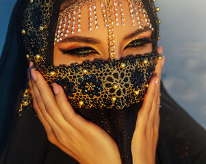 portrait close-up, young beautiful oriental woman. Beauty girl face hidden by golden veil head...