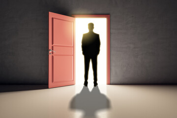 Successful business man standing in front of bright door in concrete interior with shadow on floor. Future, success and dream concept.