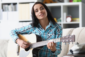 Pretty brunette woman playing on guitar in living room, female spend free time to learn new hobby