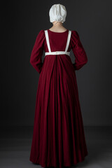 A Regency maid servant wearing a red linen dress with an apron and a cap against a studio backdrop