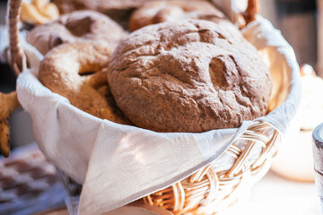 Delicious tasty gourmet freshly baked goods muffins buns, pretzel, pone, fancy rye bread, pastry in napkin towel wicker woven basket on blurred background. Bakery, bakehouse. Light day. Close up