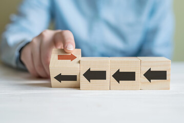 Hand flip over wooden cube block with red arrow facing the opposite direction black arrows