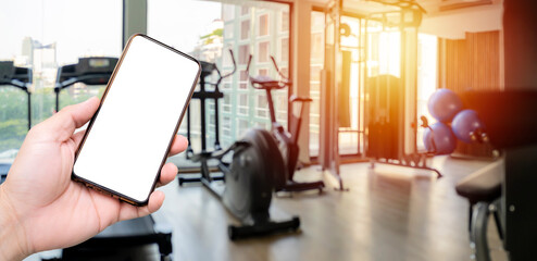Hand holding smartphone device at gym background. interior of modern fitness center gym